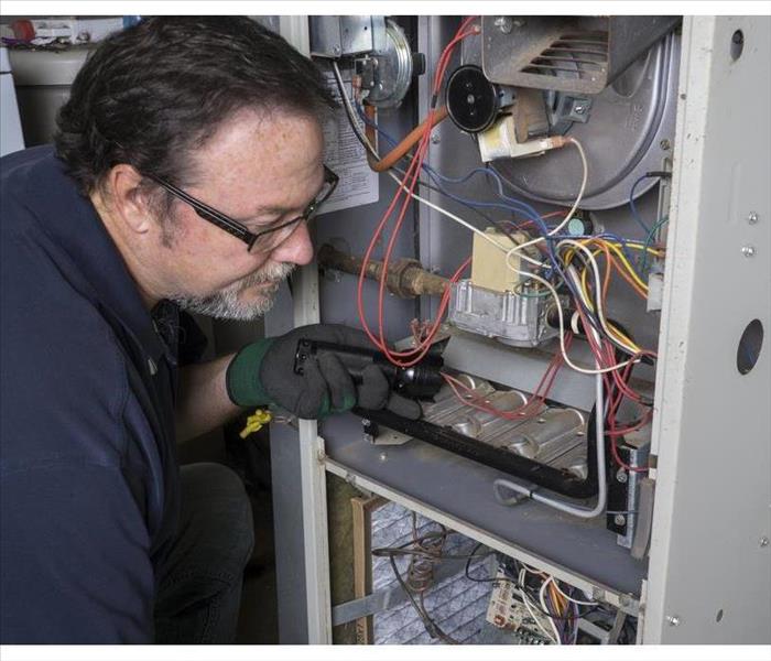 Technician looking over a gas furnace with a flashlight before cleaning it