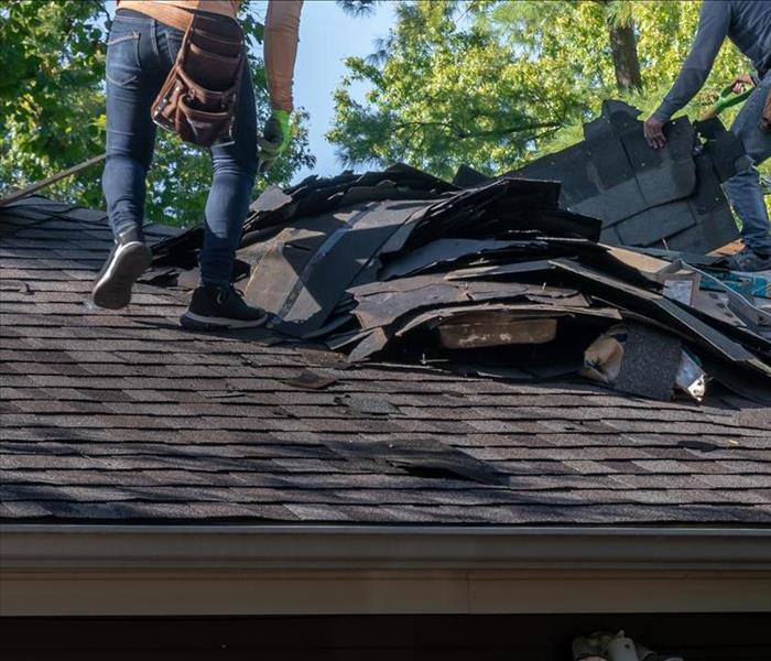 Roofers removing old material from a house in preparation for storm damage repair.